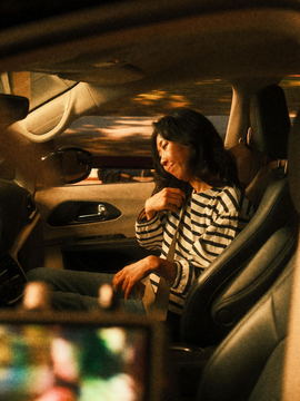 An actor in the front seat of the picture car, seen past the monitor