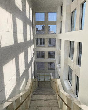 A white atrium of stacked windows with a long shadow grid across the floor