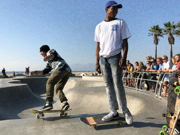 Two skateboarders at the lip of a concrete bowl by the sea