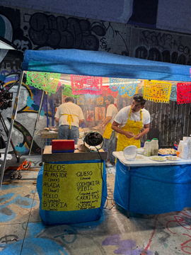 A taco stand set under a blue canopy with a hand-painted menu